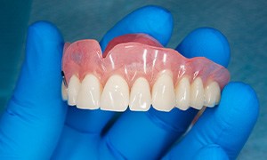 A gloved hand holding a full upper denture