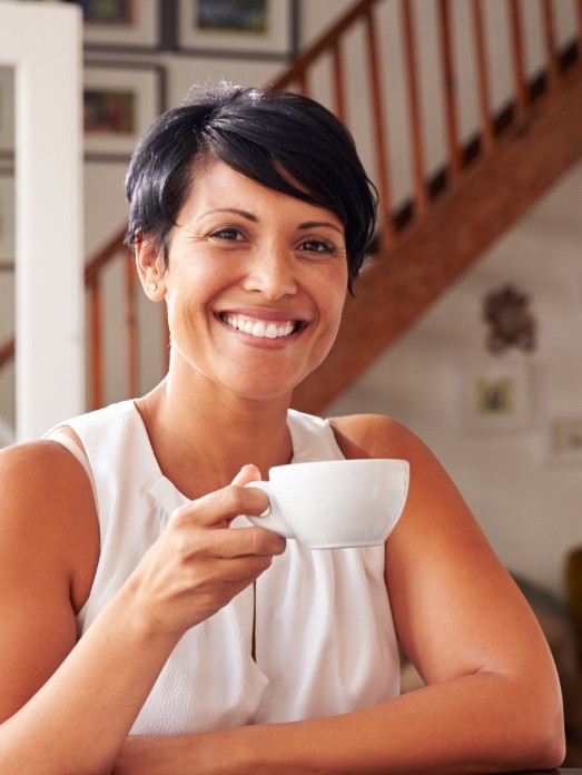 Woman holding white cup and smiling after replacing missing teeth in Rock Hill