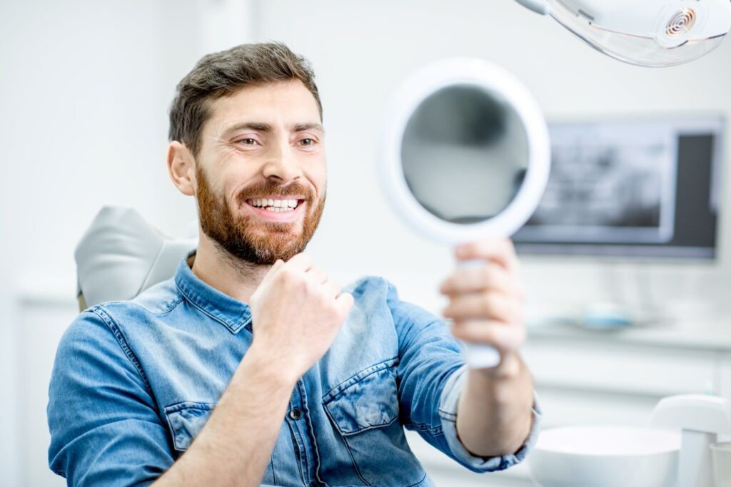 A man smiling into a mirror at the dentists office.