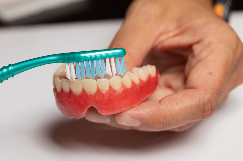 senior brushing a lower denture 